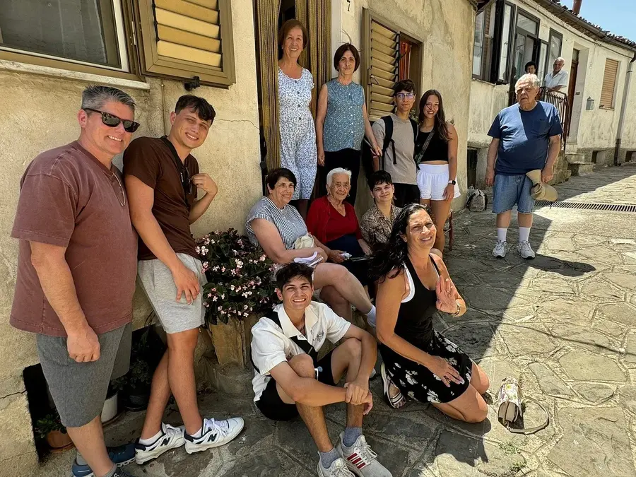 A multigenerational group gathers outside a rustic home in Alessandria del Carretto during a roots tour, capturing a heartfelt moment of family reunion and heritage exploration.